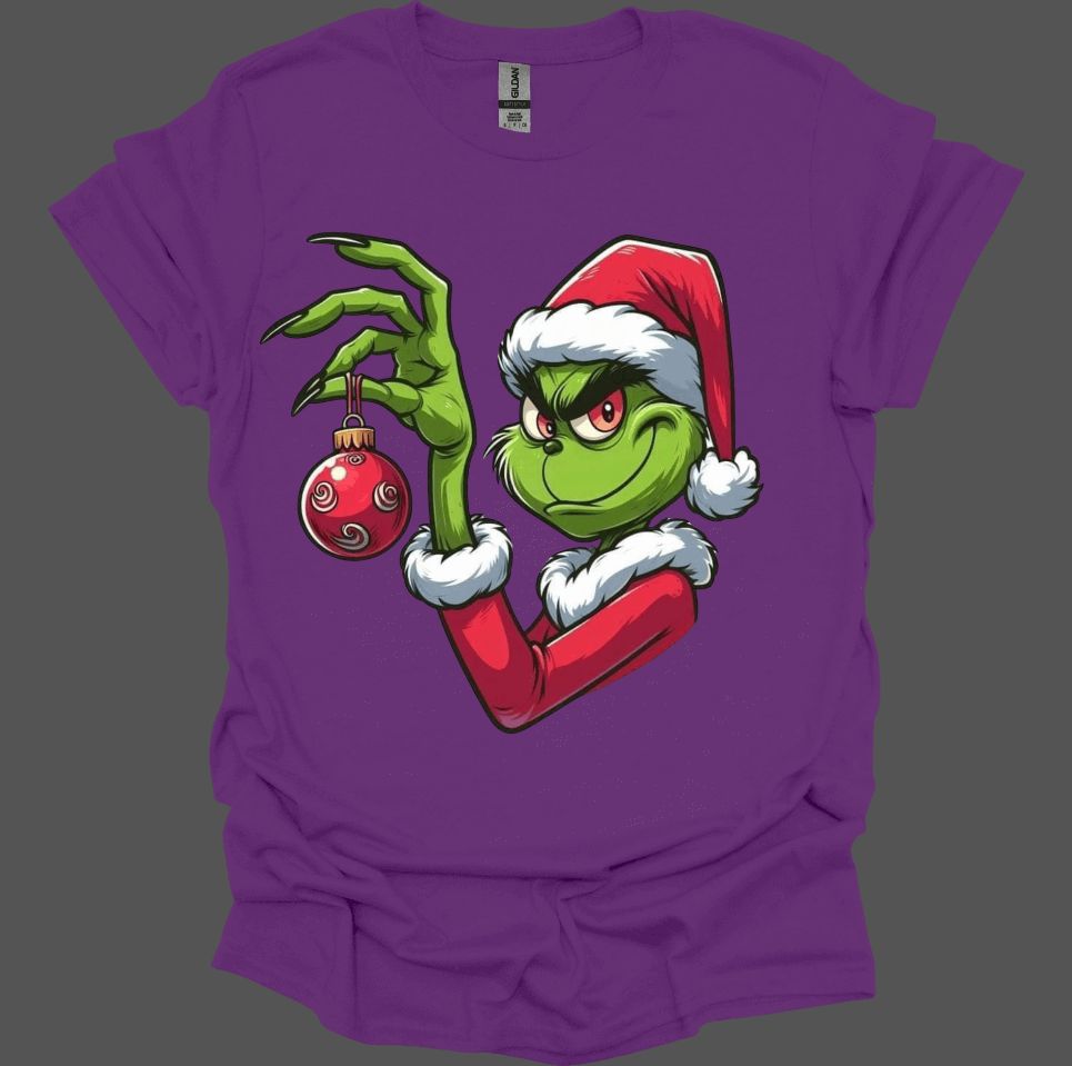 Purple Christmas With the Grinch Tee with a graphic of a character holding a Christmas ornament on a gray background