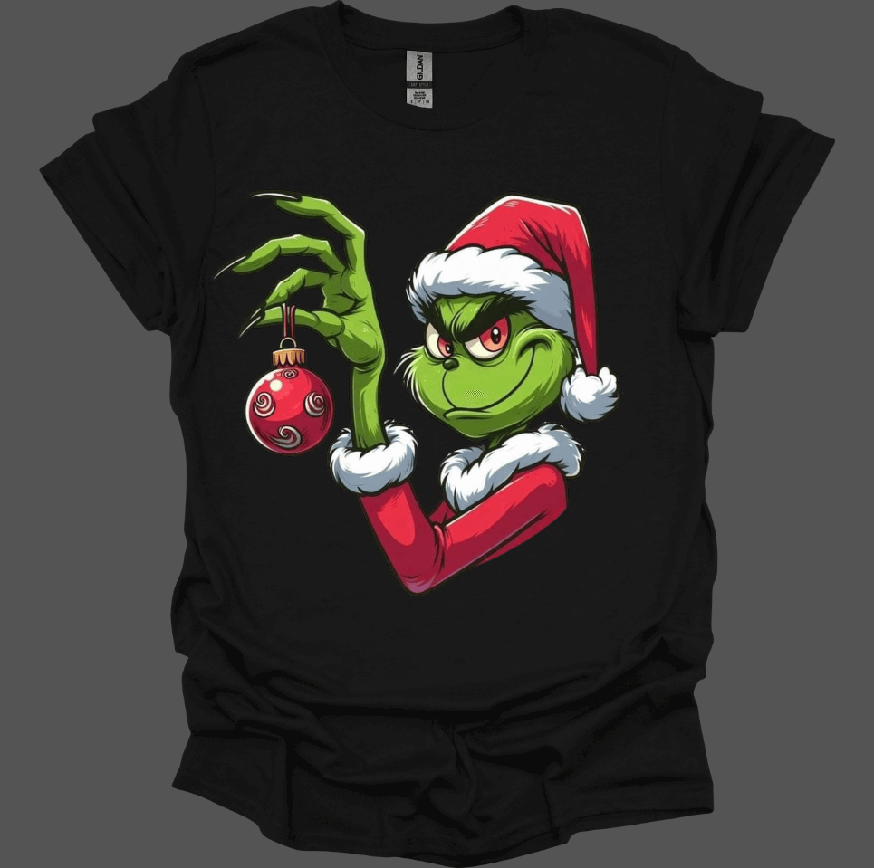 Black Christmas With the Grinch Tee with a graphic of the Grinch holding a Christmas ornament on a dark background