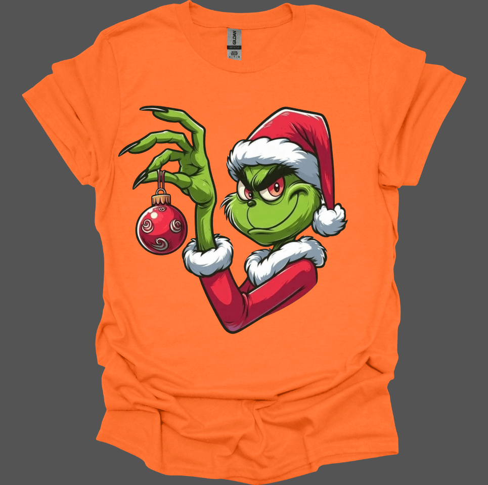 Orange Christmas With the Grinch Tee with a graphic of a character holding a Christmas ornament on a gray background